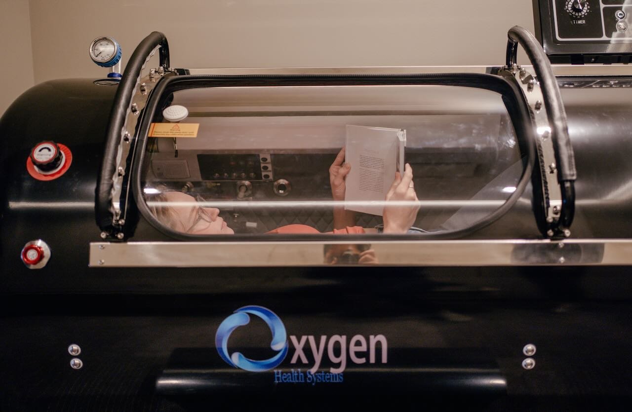 Person reading a book inside a hyperbaric chamber at Thrive Medicine Clinic, featuring professional-grade equipment for wellness-focused oxygen therapy.