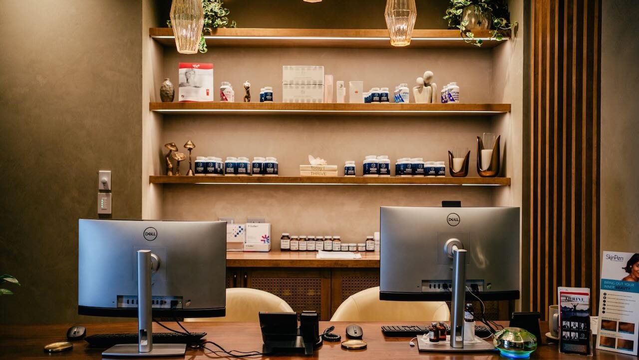 Reception area of Thrive Medicine Clinic featuring dual computer monitors, wellness products on shelves, and a modern aesthetic, emphasizing non-surgical men's health solutions.