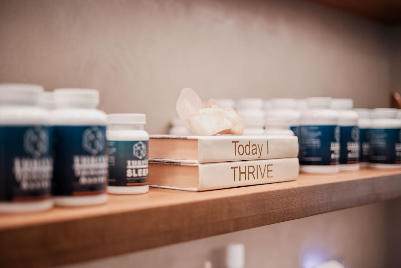 Bottles of Thrive Medicine supplements on a wooden shelf, featuring "Today I THRIVE" books and a crystal, emphasizing men's health and wellness.