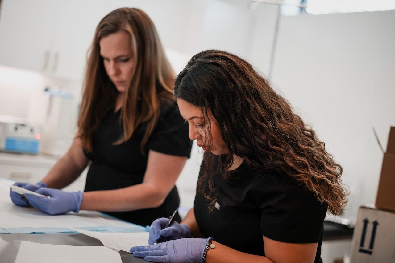 Two healthcare professionals in black scrubs, wearing gloves, examining documents and writing notes in a clinical setting, emphasizing personalized care for men's sexual health at Thrive Medicine Clinic.