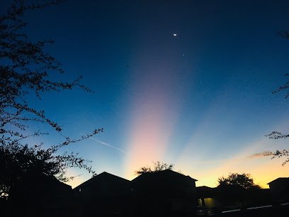 Sunset over residential houses in Houston Heights, featuring vibrant blue and orange hues with rays of light and a crescent moon in the sky.