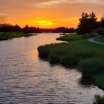 Sunset over a serene waterway with lush greenery and a winding path, reflecting the tranquil atmosphere of Sugar Land's outdoor spaces.