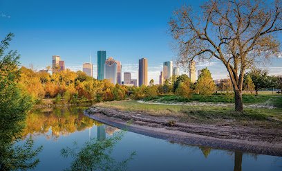 Houston skyline reflected in Buffalo Bayou, surrounded by autumn foliage and trees, highlighting the natural beauty of the Houston Heights area.