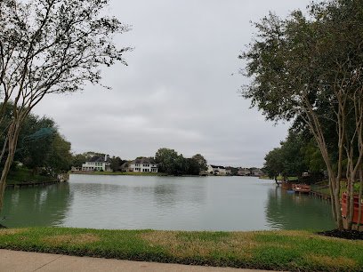 Scenic view of a calm lake surrounded by residential homes and trees in Sugar Land, Texas, reflecting a tranquil neighborhood atmosphere.