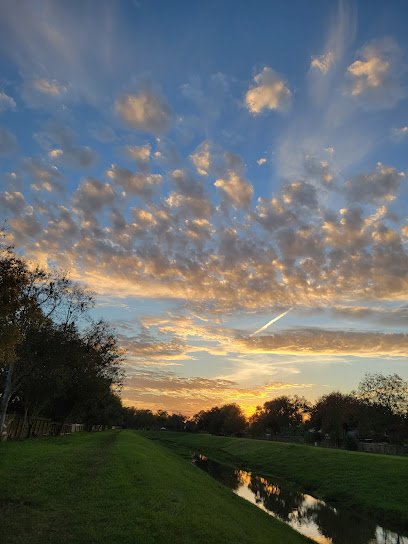 Scenic sunset over a calm waterway in Houston Heights, showcasing vibrant clouds and lush green landscape.