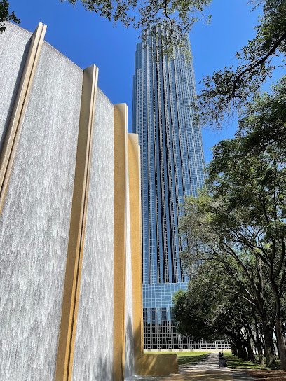Water wall and tall skyscraper in Houston Heights, surrounded by greenery and urban landscape.