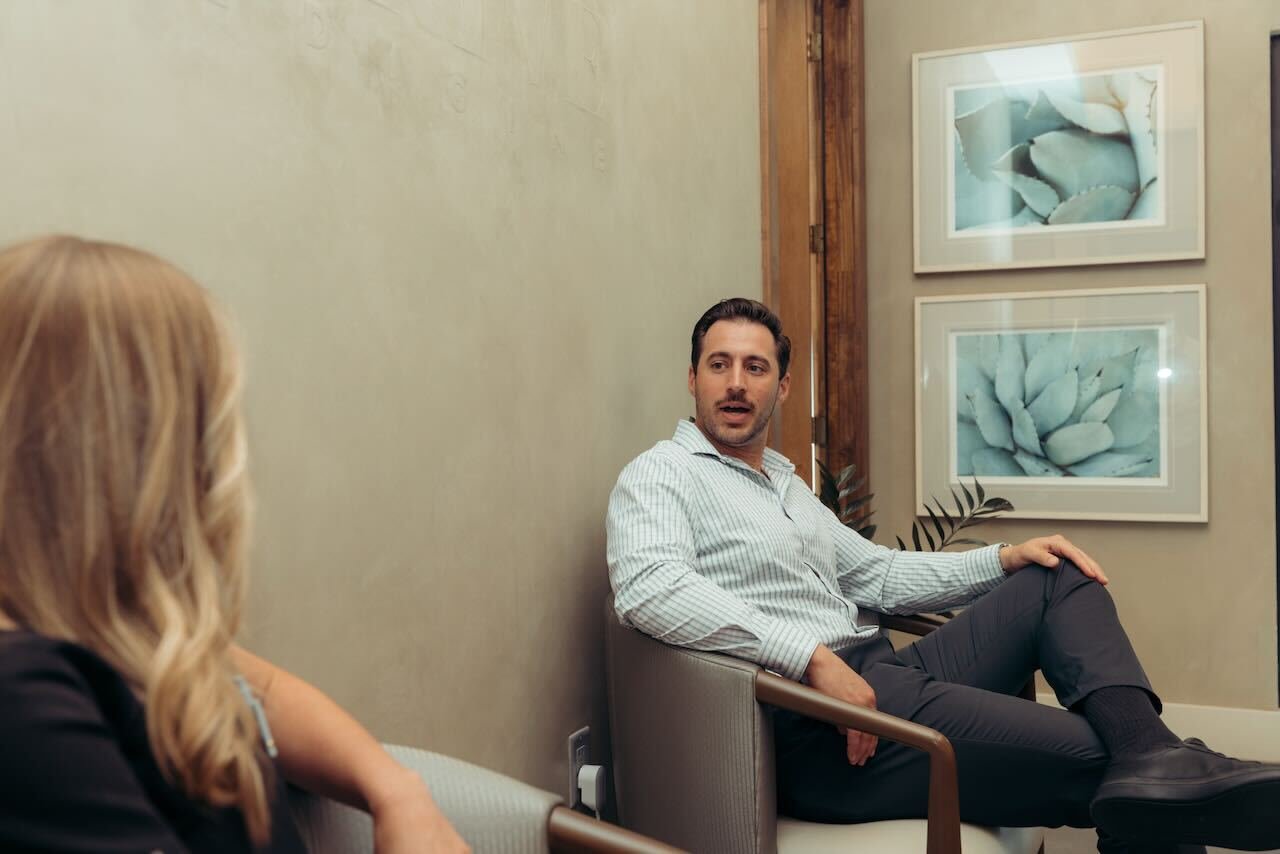 Confident middle-aged man consults with an endocrinologist about testosterone therapy in a modern Houston clinic. Bright daylight, Houston skyline, medication box, and informative pamphlet emphasize a supportive, professional men&rsquo;s health care atmosphere.